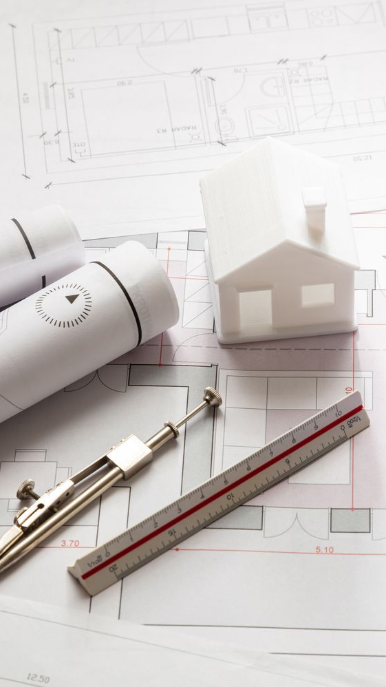 Plans architecturaux avec plans enroulés, une maison maquette, des outils de dessin.