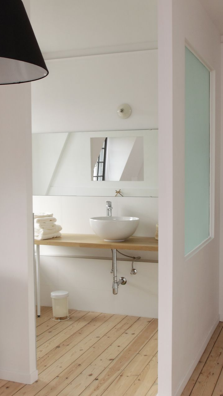 Salle de bains avec lavabo blanc, miroir, comptoir et sol en bois.