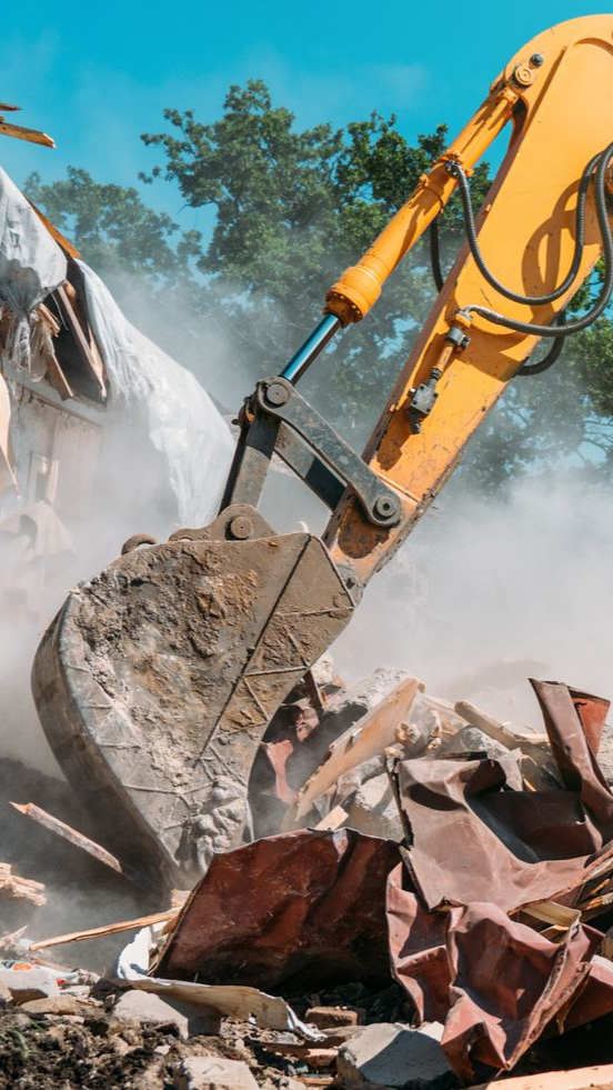 Godet jaune d'une excavatrice en train de démolir une structure, soulevant un nuage de poussière.