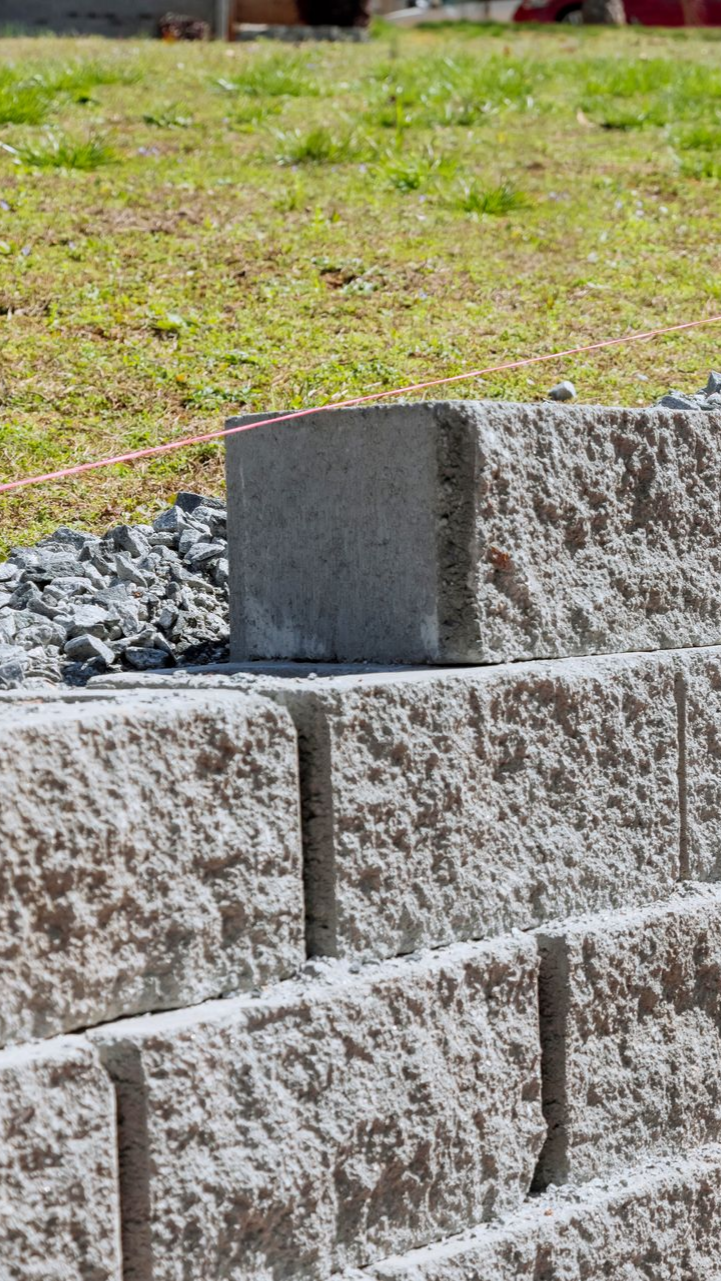 Gros plan sur un mur de soutènement en blocs de béton, avec un bloc supérieur arrondi visible.