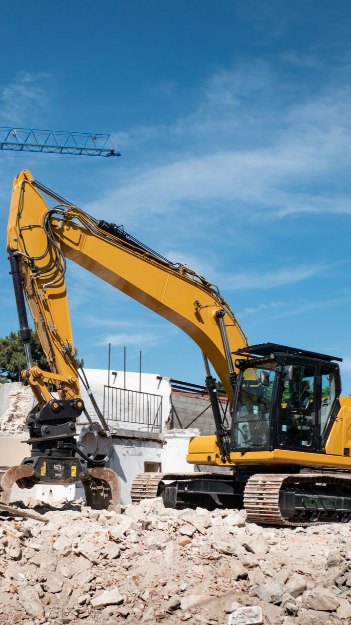 Une pelleteuse jaune démolit un bâtiment sous un ciel bleu.