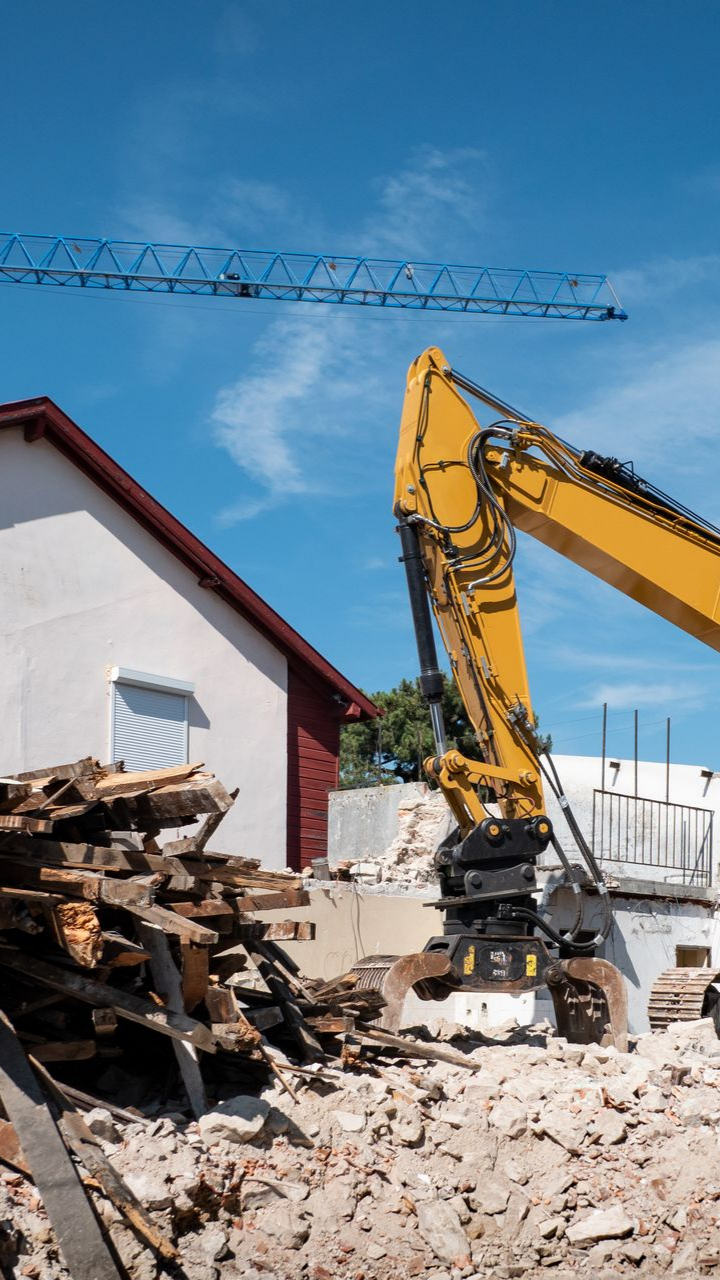 Une pelleteuse jaune démolit un bâtiment par une journée ensoleillée.
