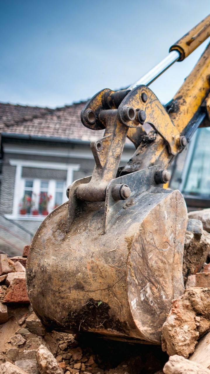 Le godet jaune d'une excavatrice ramasse des débris près d'un bâtiment sous un ciel nuageux.