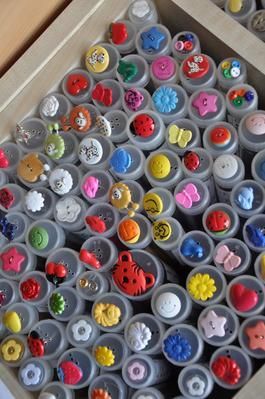 Sortiment bunter Dekoknöpfe, aufbewahrt in kleinen, durchsichtigen Röhrchen in einer rechteckigen Schachtel.