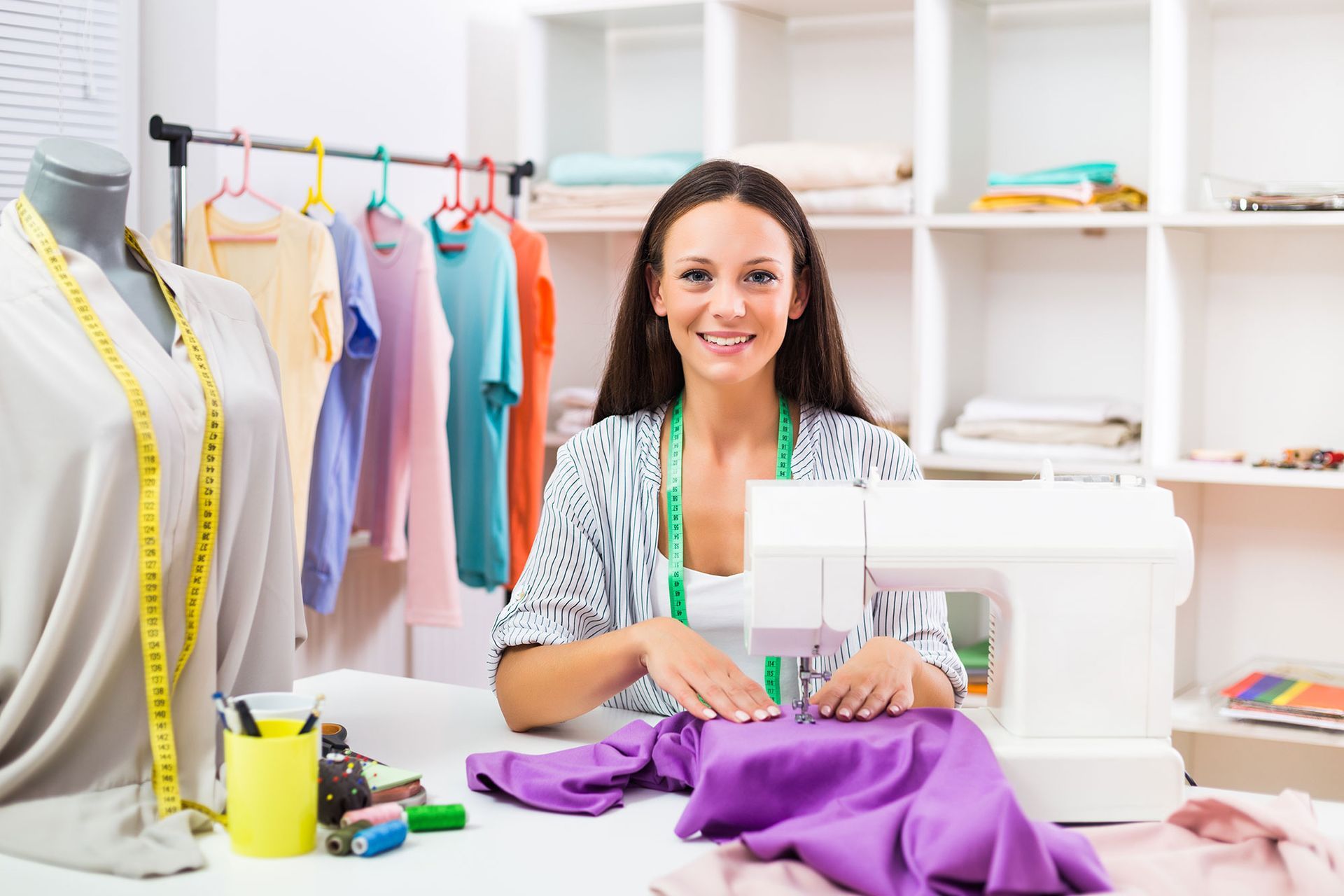 Frau näht lila Stoff an einem Tisch in einem hellen Nähstudio.