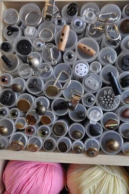 Knöpfe werden in durchsichtigen Röhren in einem hölzernen Organizer aufbewahrt, darunter liegt Garn.