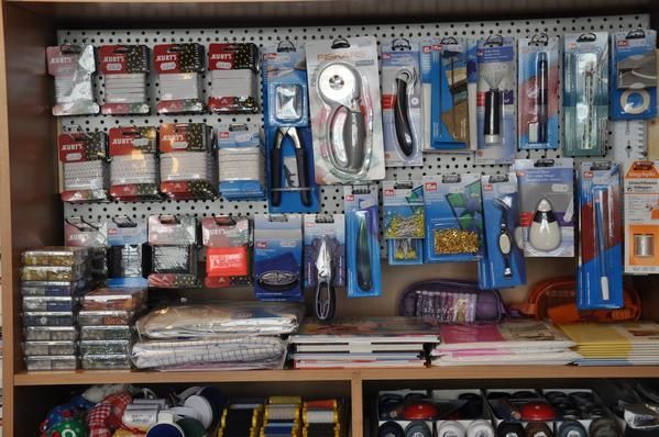 Bastelbedarf in einem Verkaufsregal, darunter Scheren, Rollschneider und andere verpackte Werkzeuge.