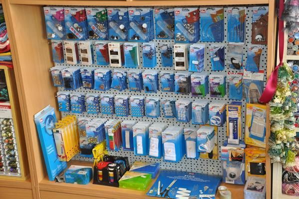 Ausstellung verpackter Elektronik in einem Geschäft, überwiegend blau und weiß, auf einem Holzregal mit Stecktafelrückwand.