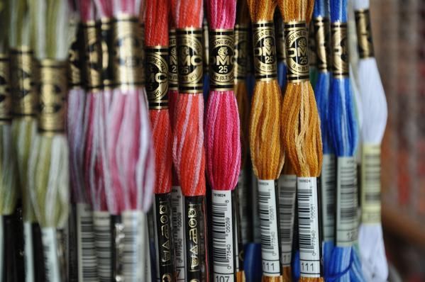 Ausgestellt sind bunte Stickgarnbündel, sortiert nach Farbe: Rosa, Orange, Gelb, Blau.