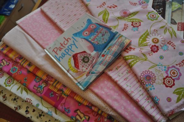 Stoffreste und ein Buch mit dem Titel „Patch happy!“ in Rosa-, Orangetönen und Blumenmustern.