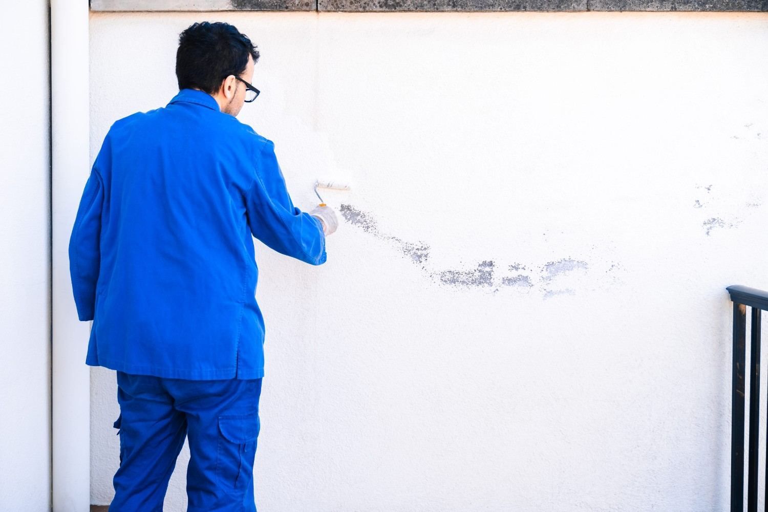 Persona con chaqueta azul limpiando una pared blanca con un paño.