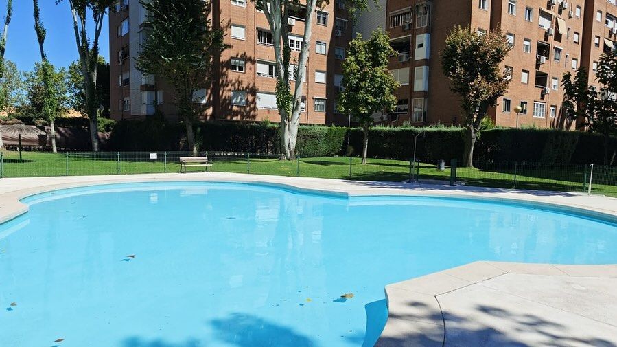 Piscina al aire libre junto a edificios de apartamentos en un día soleado.