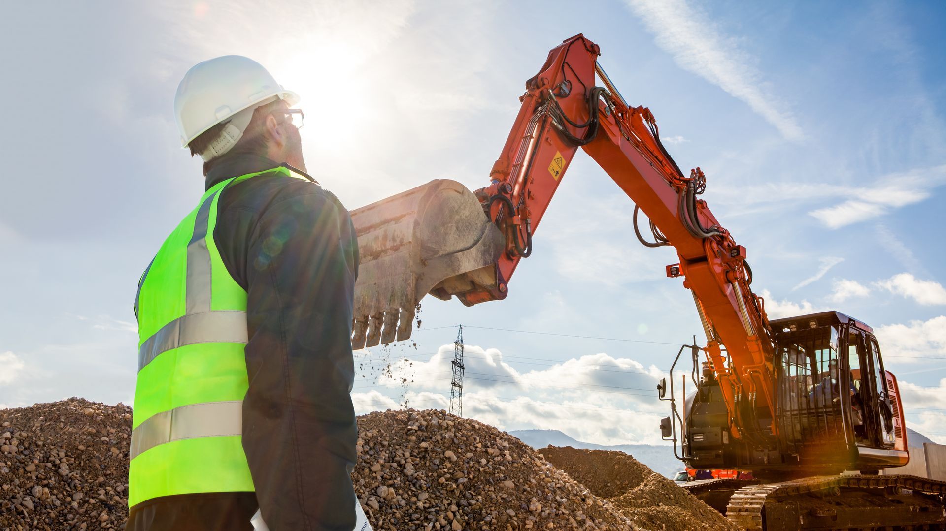 Un trabajador de la construcción está parado frente a una excavadora en un sitio de construcción.