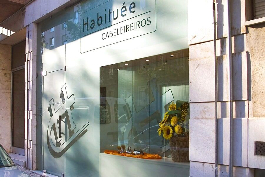 Fachada de salão de cabeleireiro com vitrine de vidro fosco, logotipo e arranjo de flores.