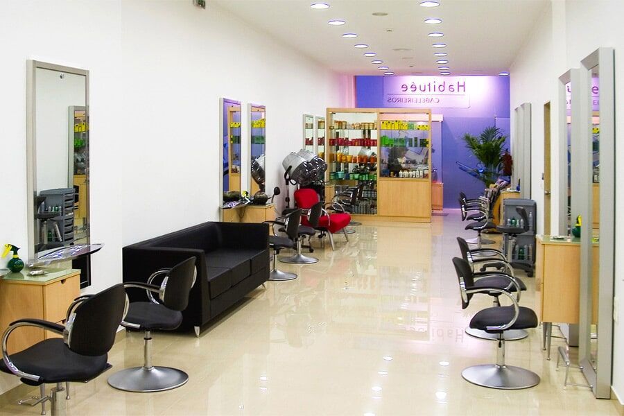 Interior de um salão de cabeleireiro com espelhos, cadeiras de cabeleireiro, área de espera e expositores de produtos.