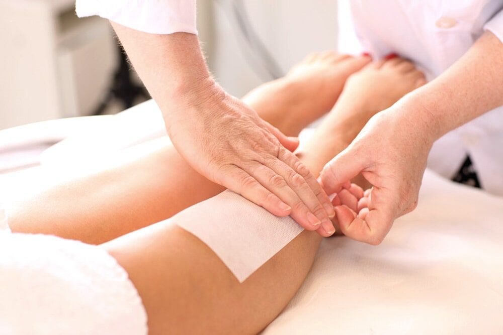 Perna sendo depilada em um salão; pessoa aplicando uma tira de cera na perna.