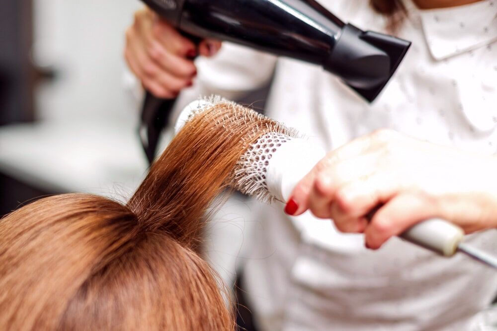 Cabeleireira usando uma escova redonda e um secador de cabelo para modelar o cabelo .