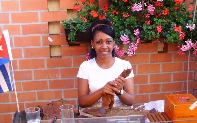 Une femme est assise à une table en train de fabriquer des cigares avec un drapeau cubain en arrière-plan
