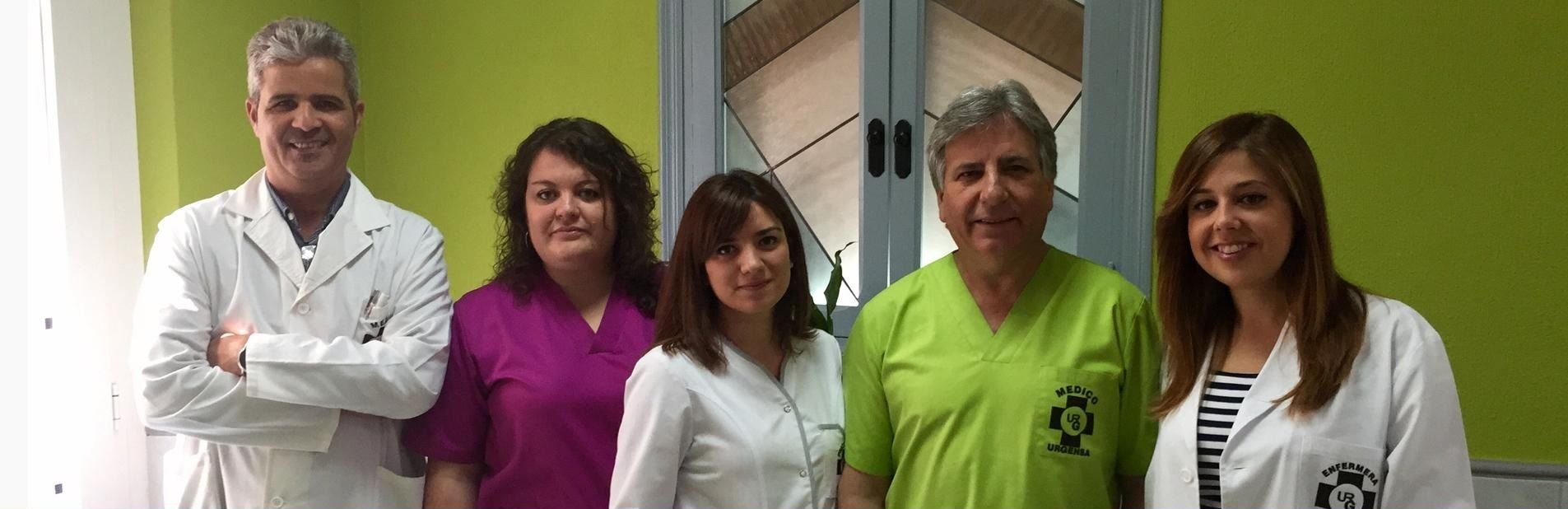 Cinco personas de pie en el interior, sonriendo, con uniformes médicos blancos y de color verde brillante.