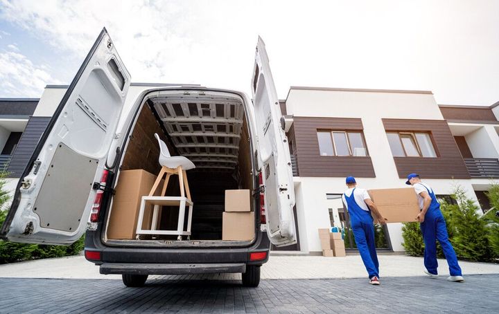 Dos transportistas están cargando cajas en una camioneta frente a una casa.