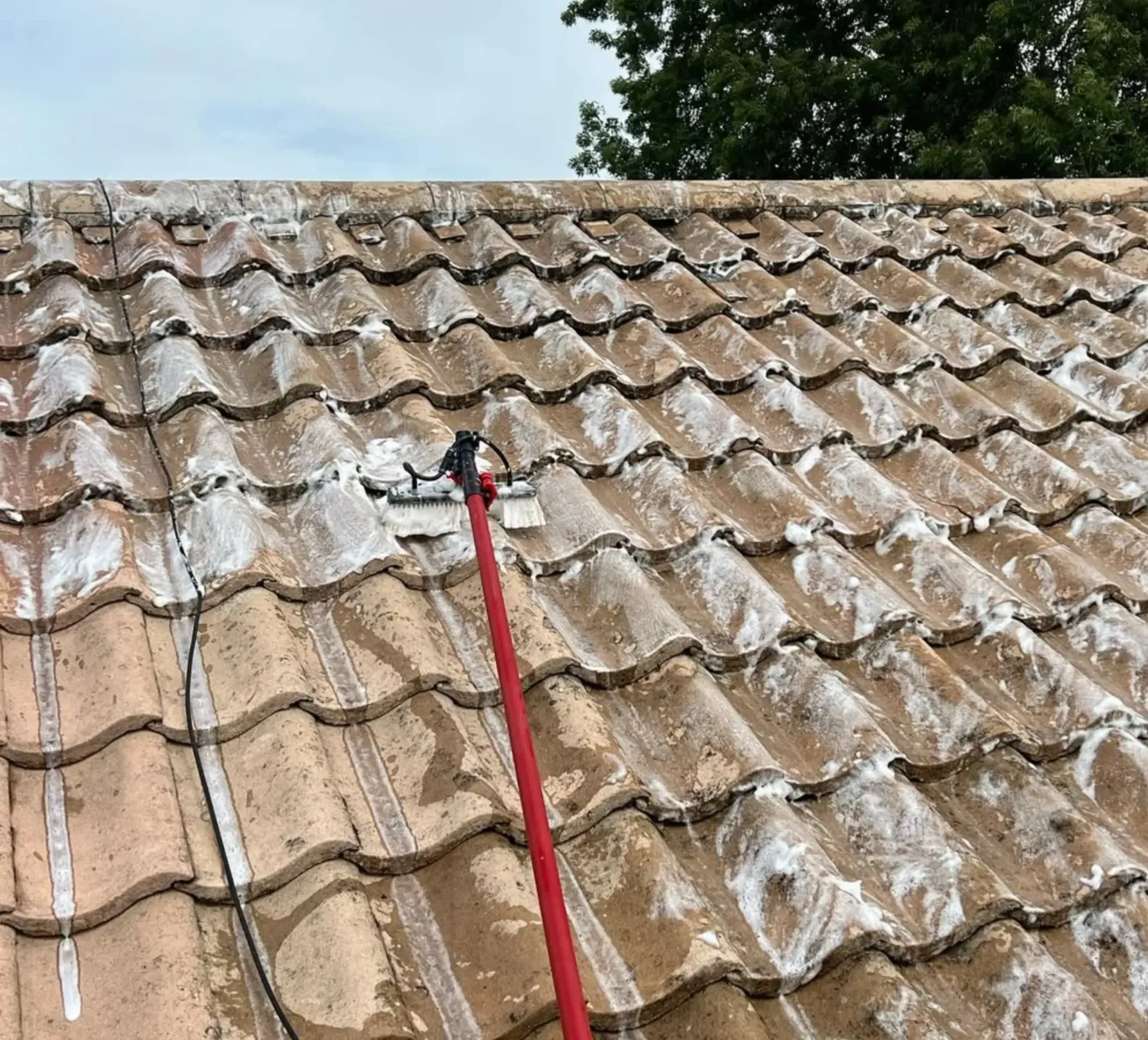 Roof tiles being cleaned with a red hose or pressure washer wand.