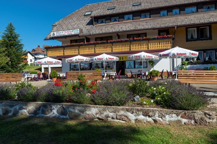 Ein großes Gebäude mit vielen Sonnenschirmen und Stühlen davor | Hotel-Restaurant SchöpPerle