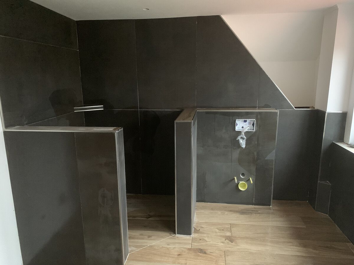 Ein Badezimmer mit schwarzen Fliesen und Holzboden wird renoviert.