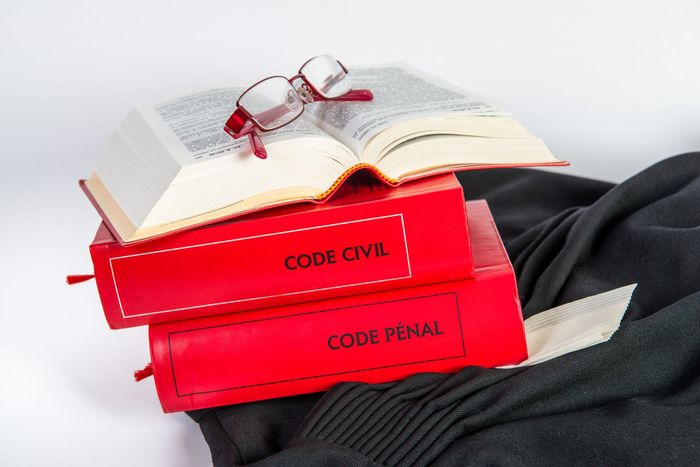 Une pile d'ouvrages juridiques dont un Code civil et un Code pénal avec une paire de lunettes et une robe d'avocat