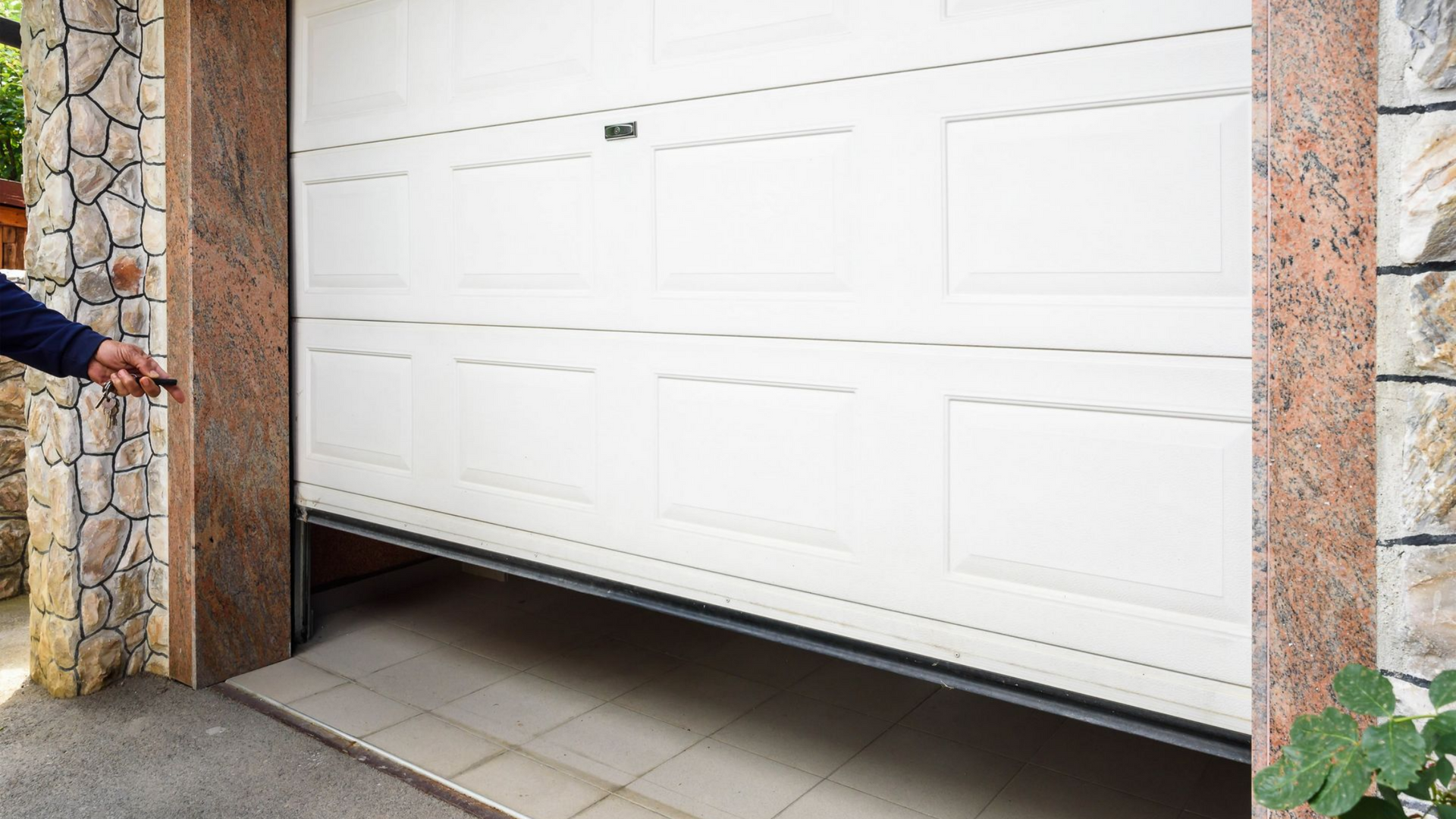 Porte de garage sectionnelle blanche installée sur une façade en pierre