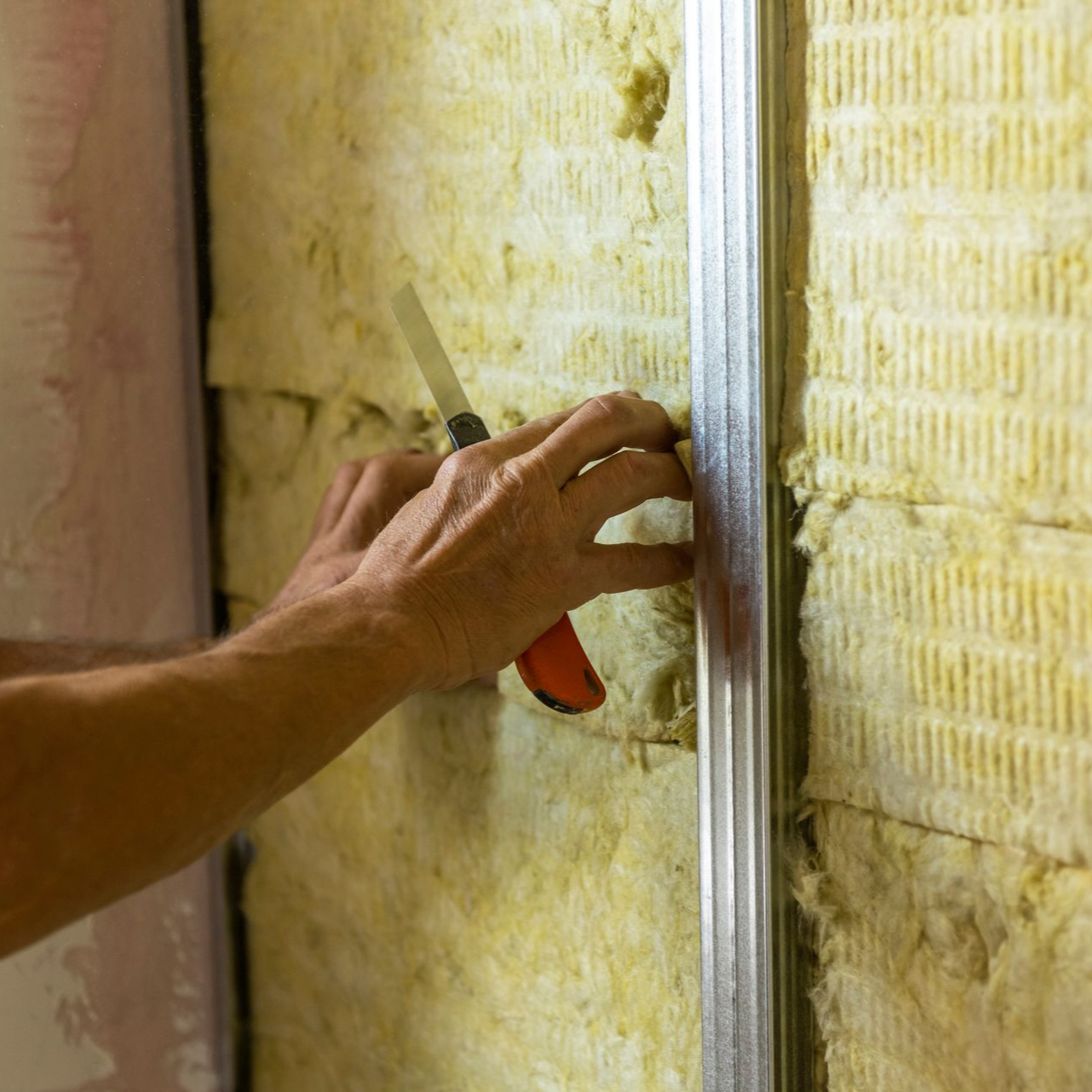 Mains posant de la laine minérale sur une structure en bois