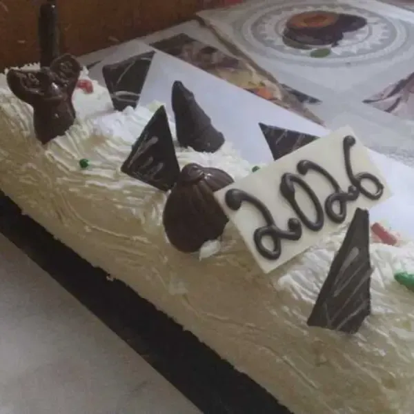 Un tronco de Navidad cubierto de crema pastelera, decorado con diversos adornos de chocolate y una inscripción 