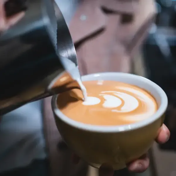 Un barista vierte leche vaporizada en una taza de cerámica color canela para crear un dibujo artístico en el café con leche.
