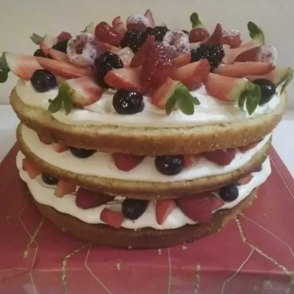 Un bizcocho de tres capas con glaseado blanco y cobertura de fresas frescas, frambuesas y frutos rojos oscuros.