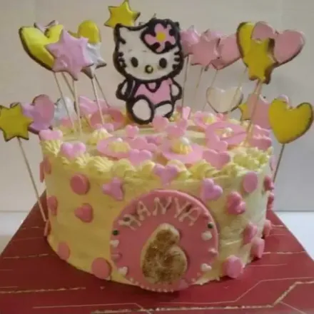 Una tarta de cumpleaños amarilla glaseada, decorada con una figura de Hello Kitty, detalles de corazones y estrellas