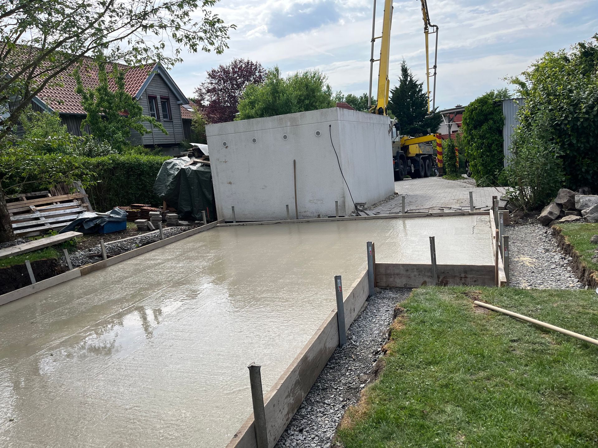 Im Hintergrund wird eine Betoneinfahrt gegossen, ein Kran ist zu sehen.