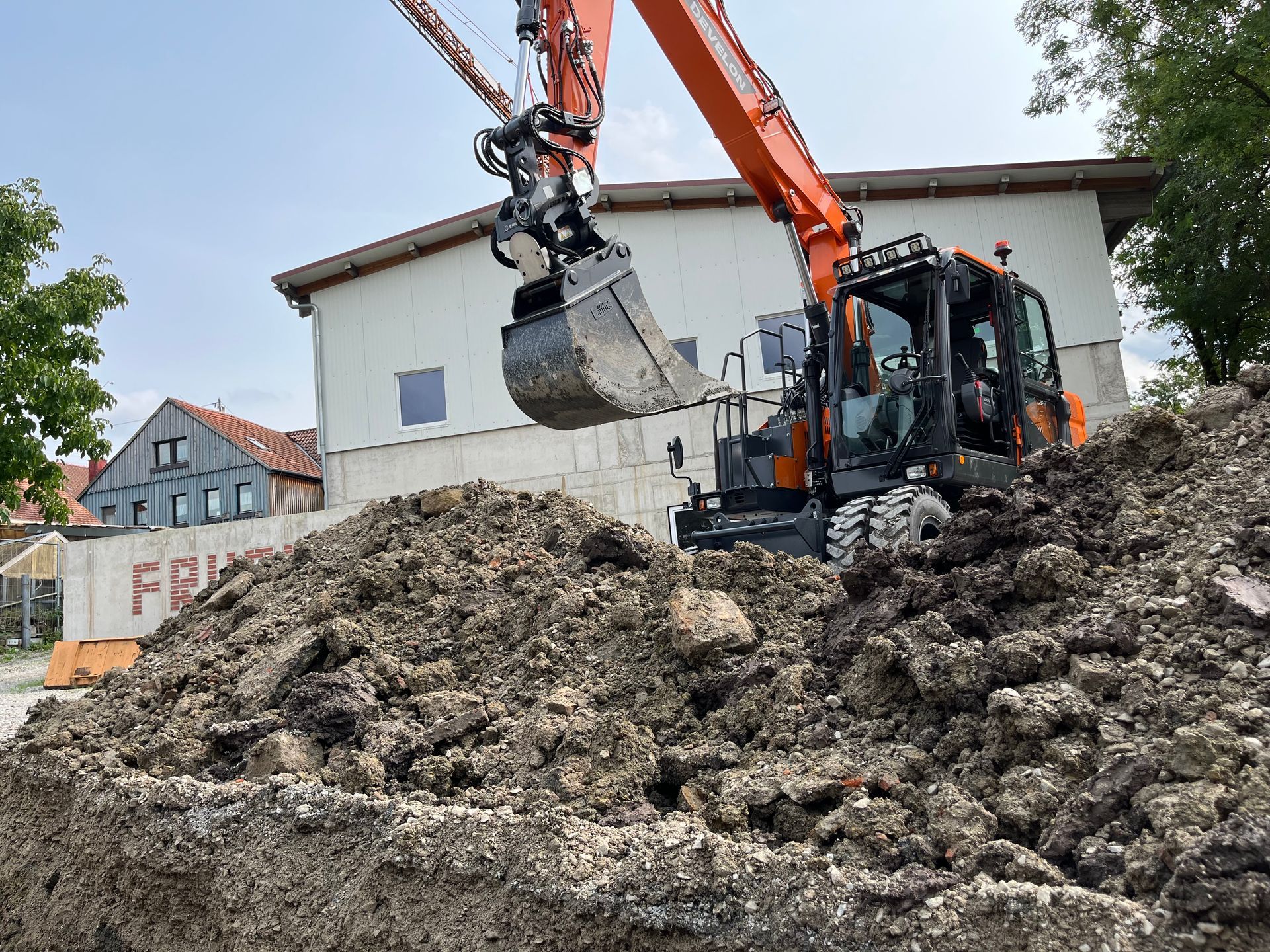 Ein Bagger gräbt einen Erdhaufen vor einem Gebäude aus.