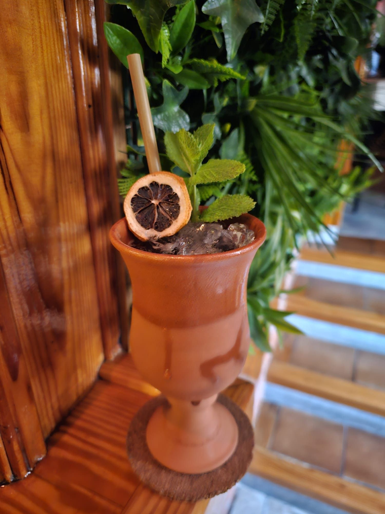 Un cóctel servido en una copa de terracota, adornado con una rodaja de cítricos secos y menta fresca, sobre una superficie de madera.