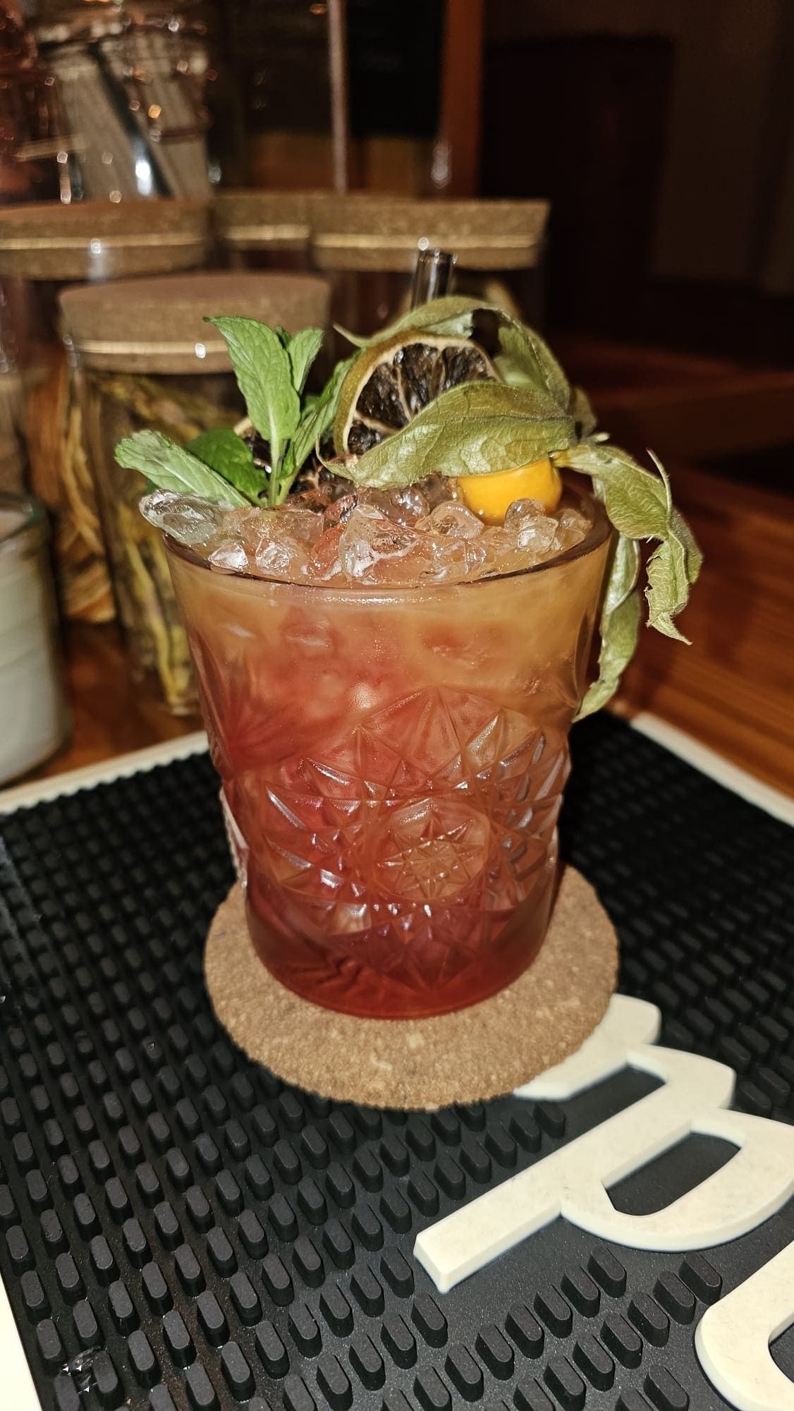 Un cóctel decorativo servido en un vaso texturizado lleno de hielo picado, coronado con menta fresca y una fruta de physalis.