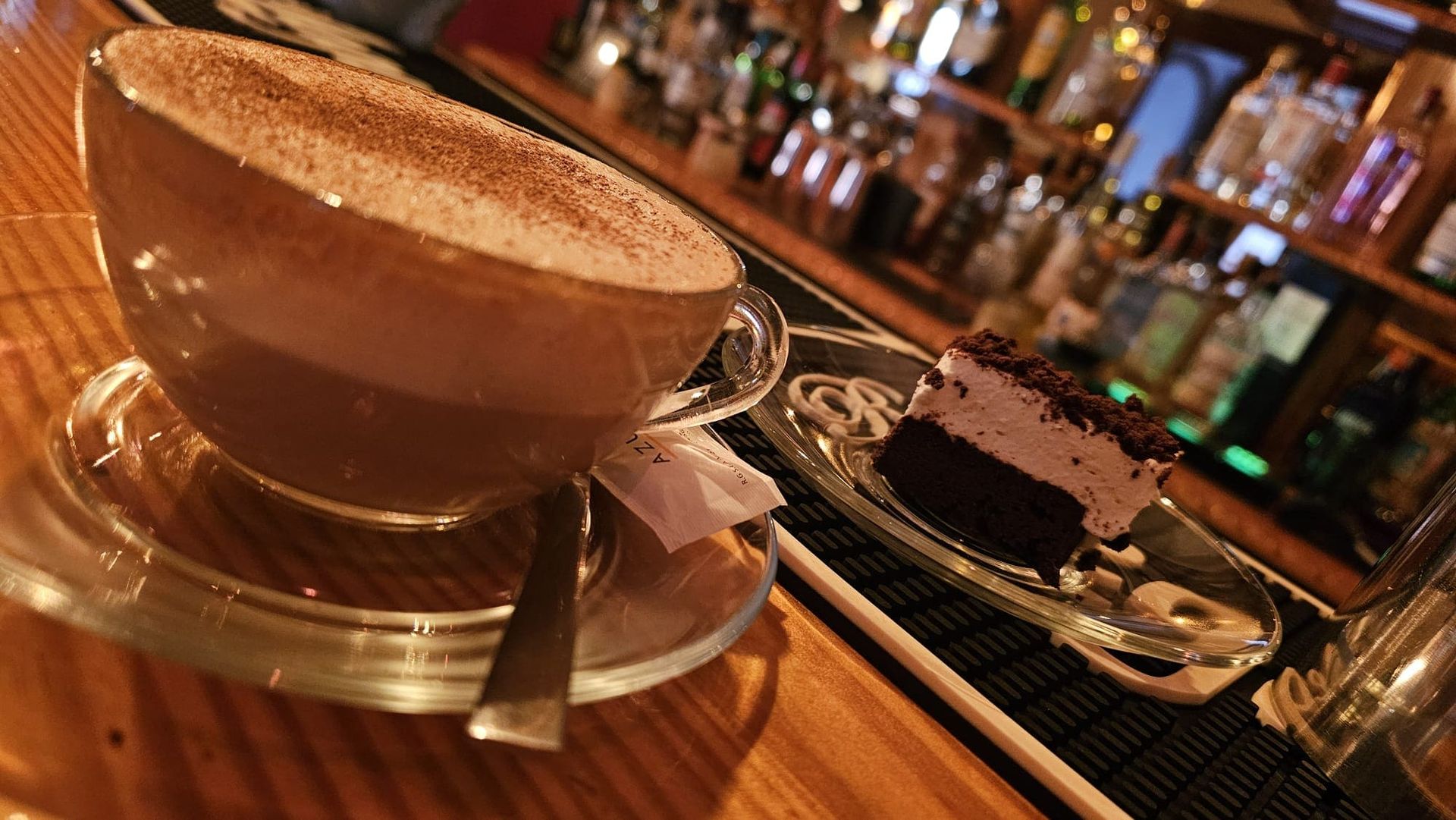 Una taza de café espolvoreada con cacao y una porción de pastel de chocolate reposan sobre una barra de madera.