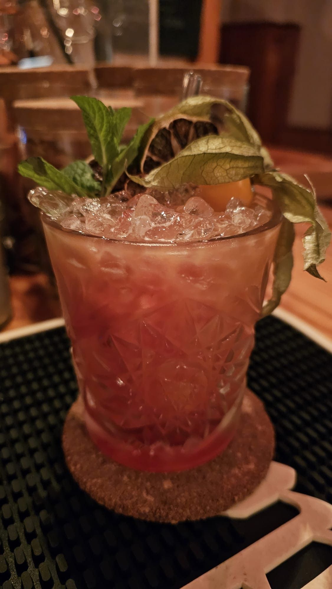 Un cóctel servido en un vaso grabado, lleno de hielo picado y adornado con una ramita de menta, una rodaja de lima seca y una cáscara.