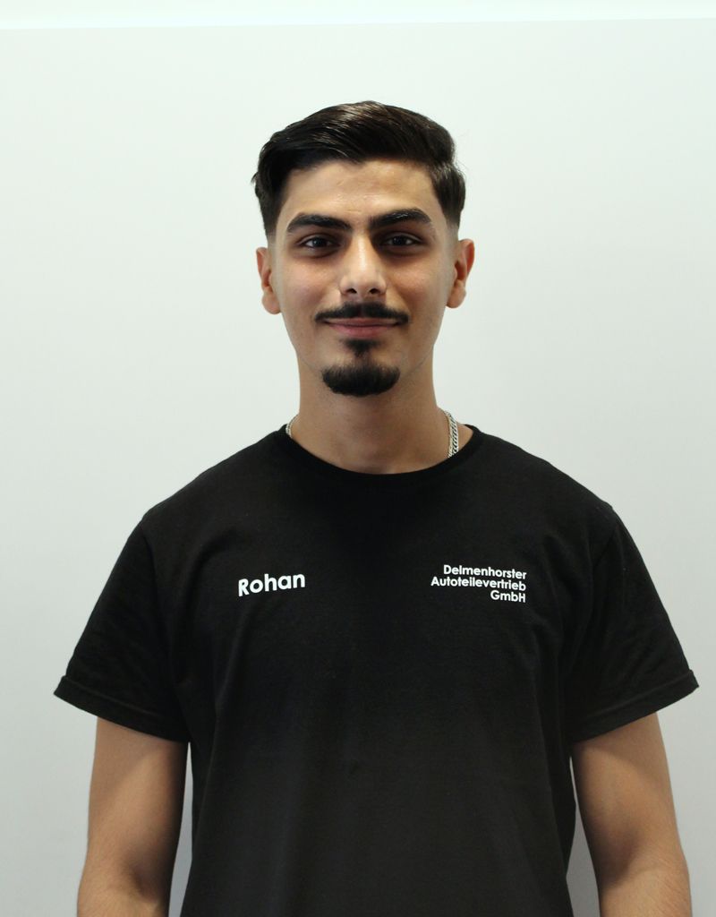 Junger Mann in schwarzem T-Shirt mit Text, posiert vor einer weißen Wand.