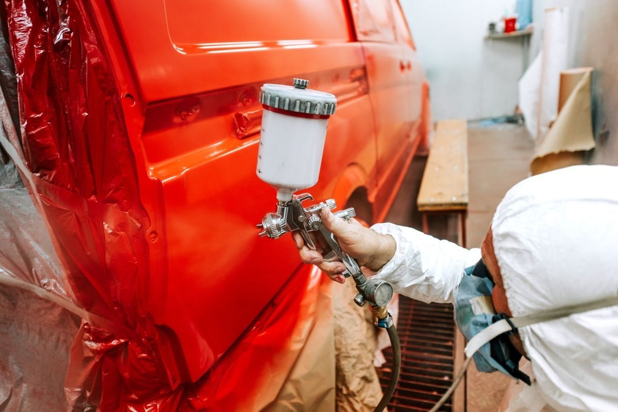 Un hombre está pintando con aerosol una camioneta roja en un garaje.