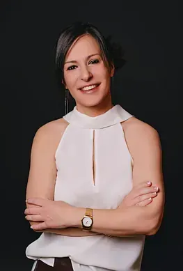 Una mujer que viste una camiseta blanca y un reloj está de pie con los brazos cruzados.