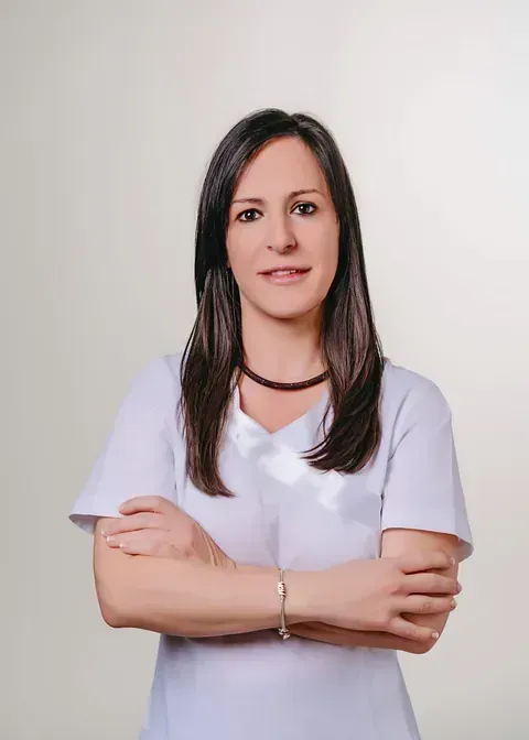 Una mujer con una camisa blanca está de pie con los brazos cruzados.