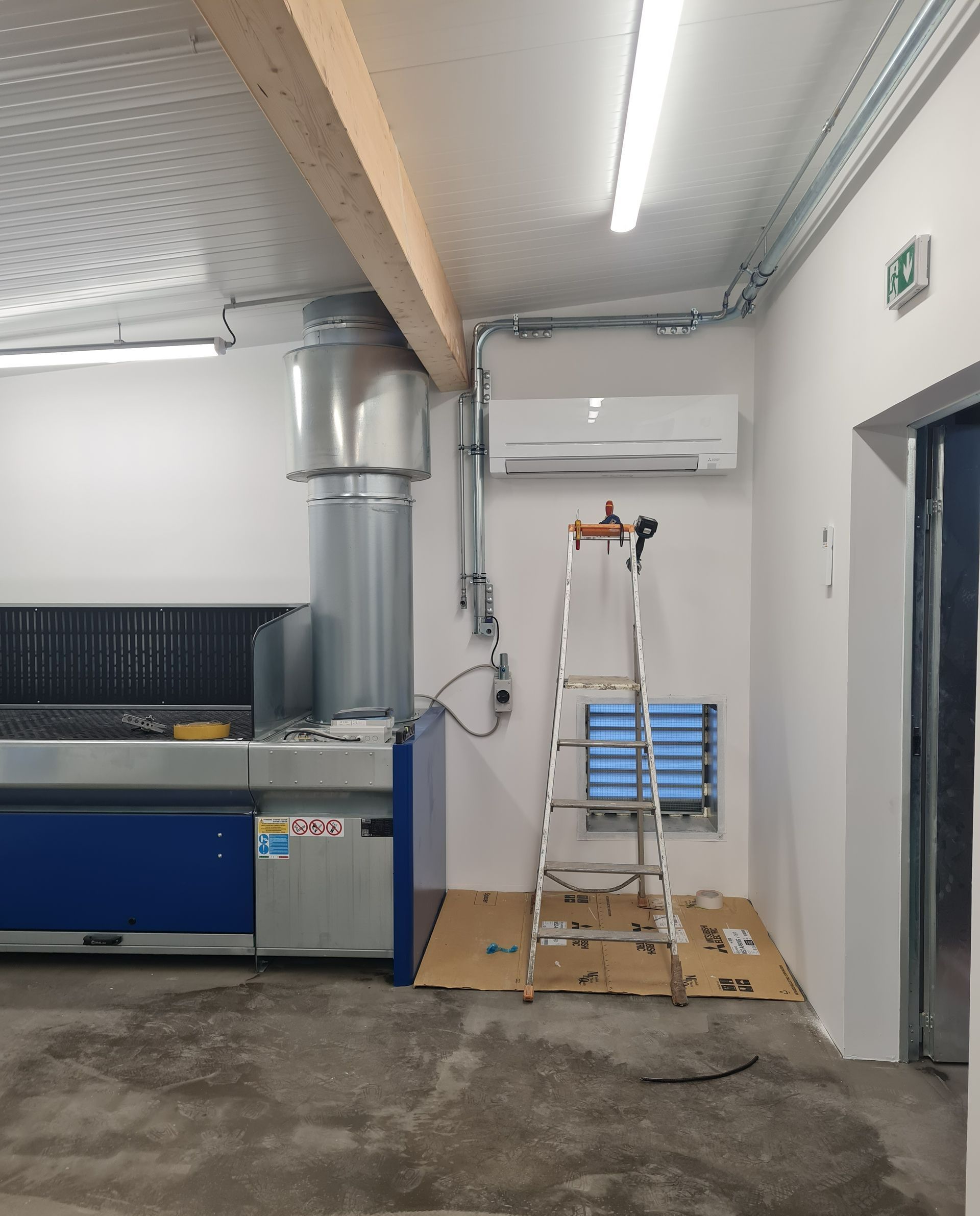 Espace professionnel avec à droite une échelle sous une climatisation murale en cours d'installation
