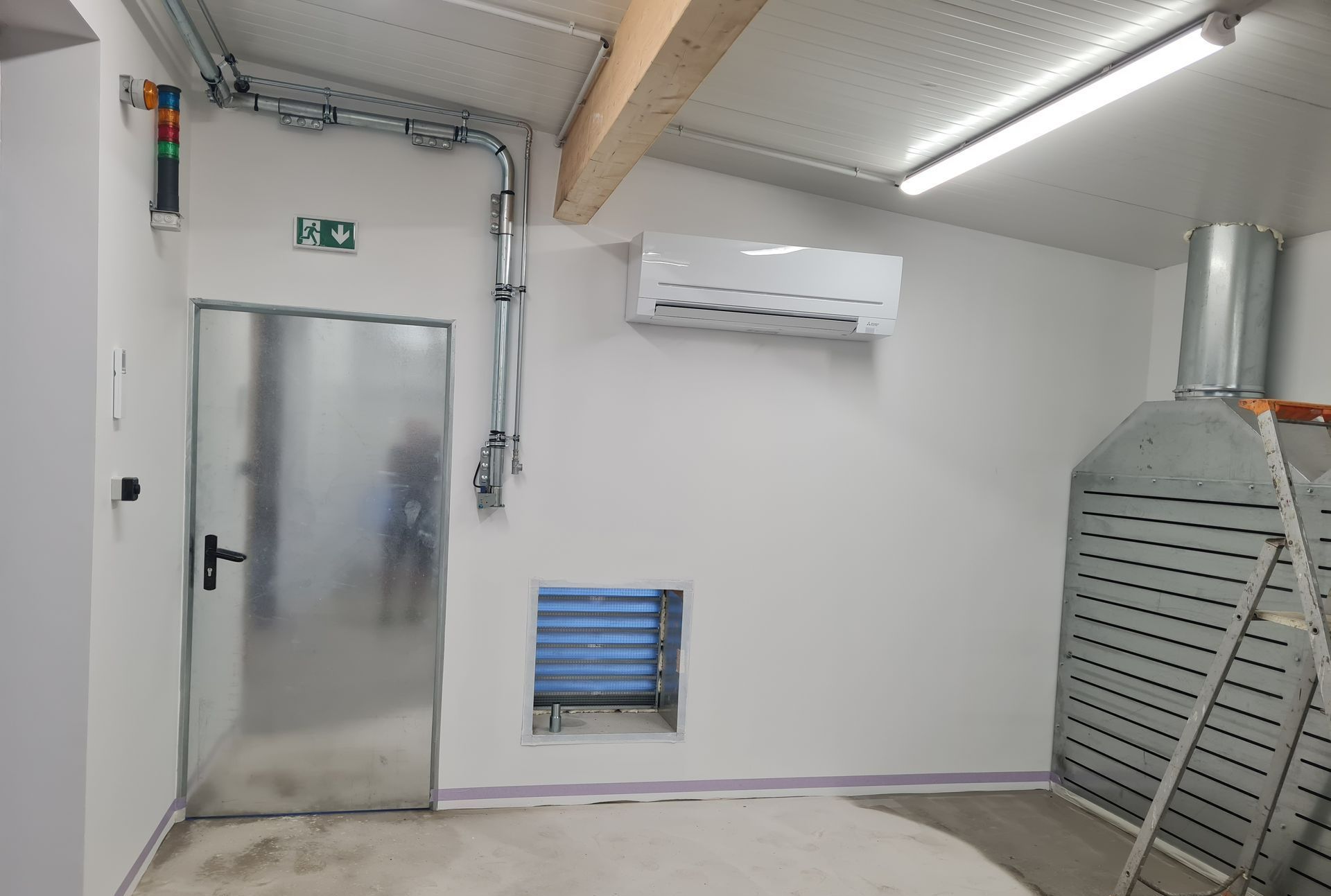 Un espace avec une porte métallique à gauche, une évacuation en tôle à droite, et une climatisation murale en haut