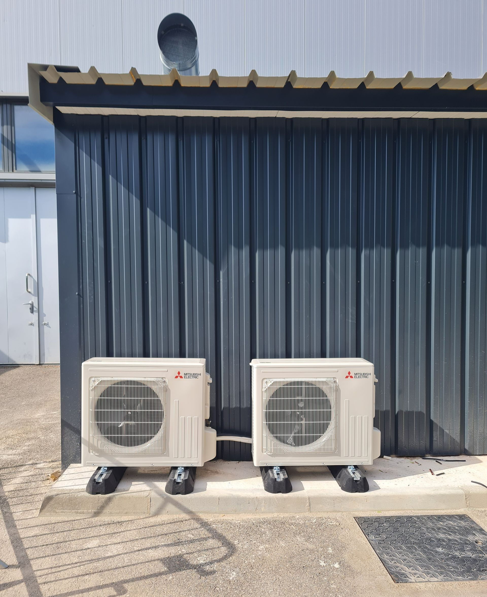 Deux unités extérieurs d'une pompe à chaleur côte à côte sur un toit devant un mur de tôle bleu