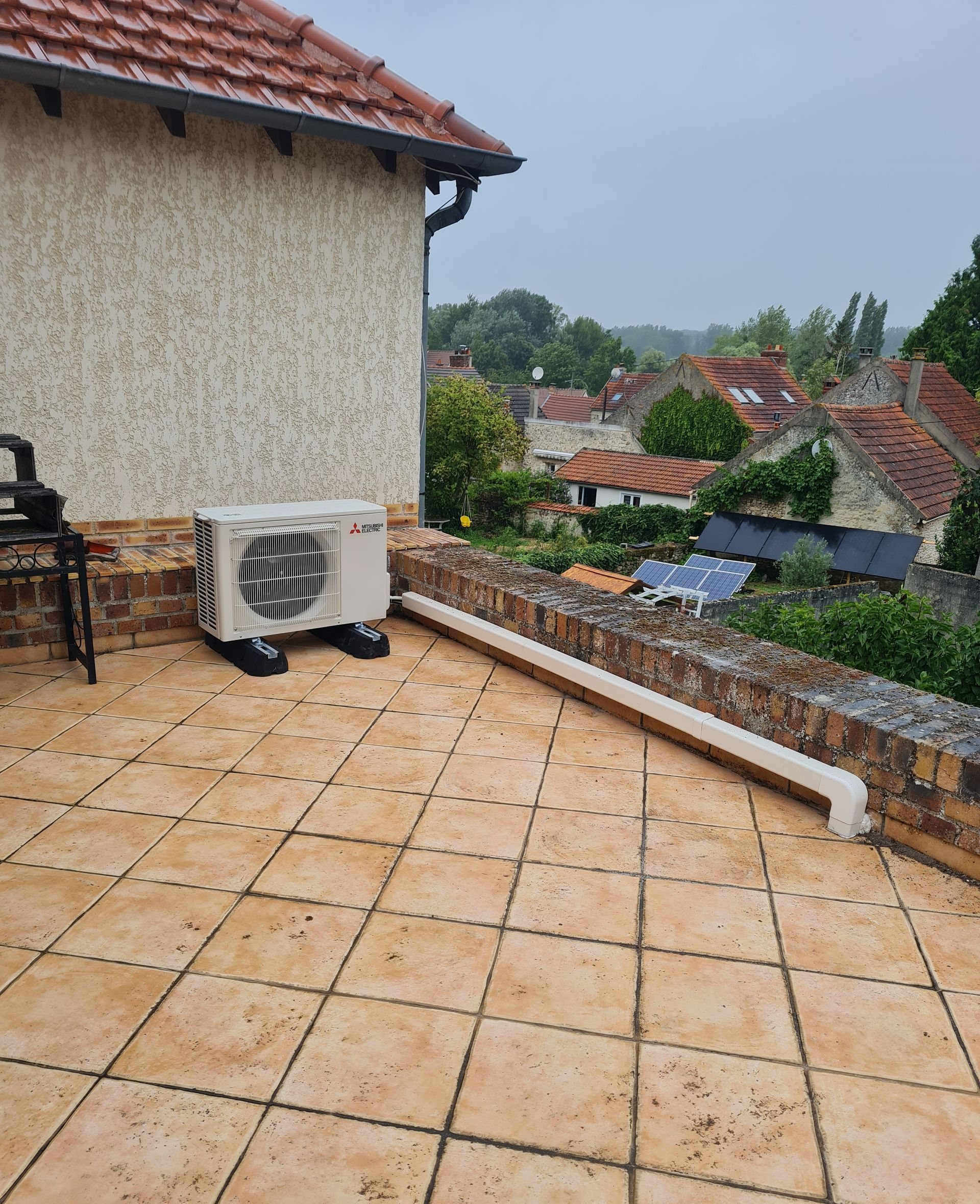 Unité extérieur d'une pompe à chaleur air-air installée sur un toit, et cache-cables le long du muret à droite