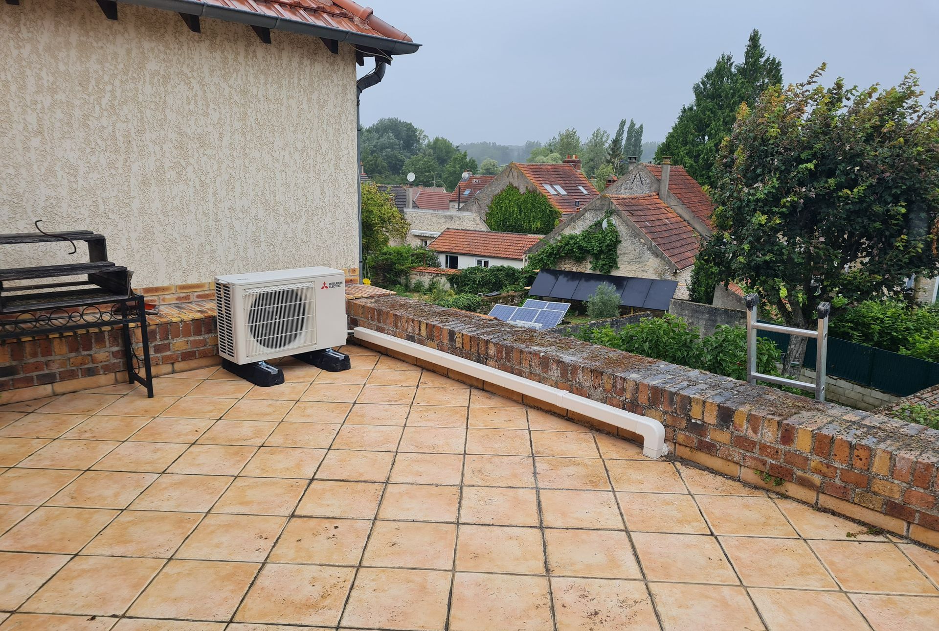 Vue large d'une unité extérieur de pompe à chaleur sur un toit, et cache-cables le long du muret à droite