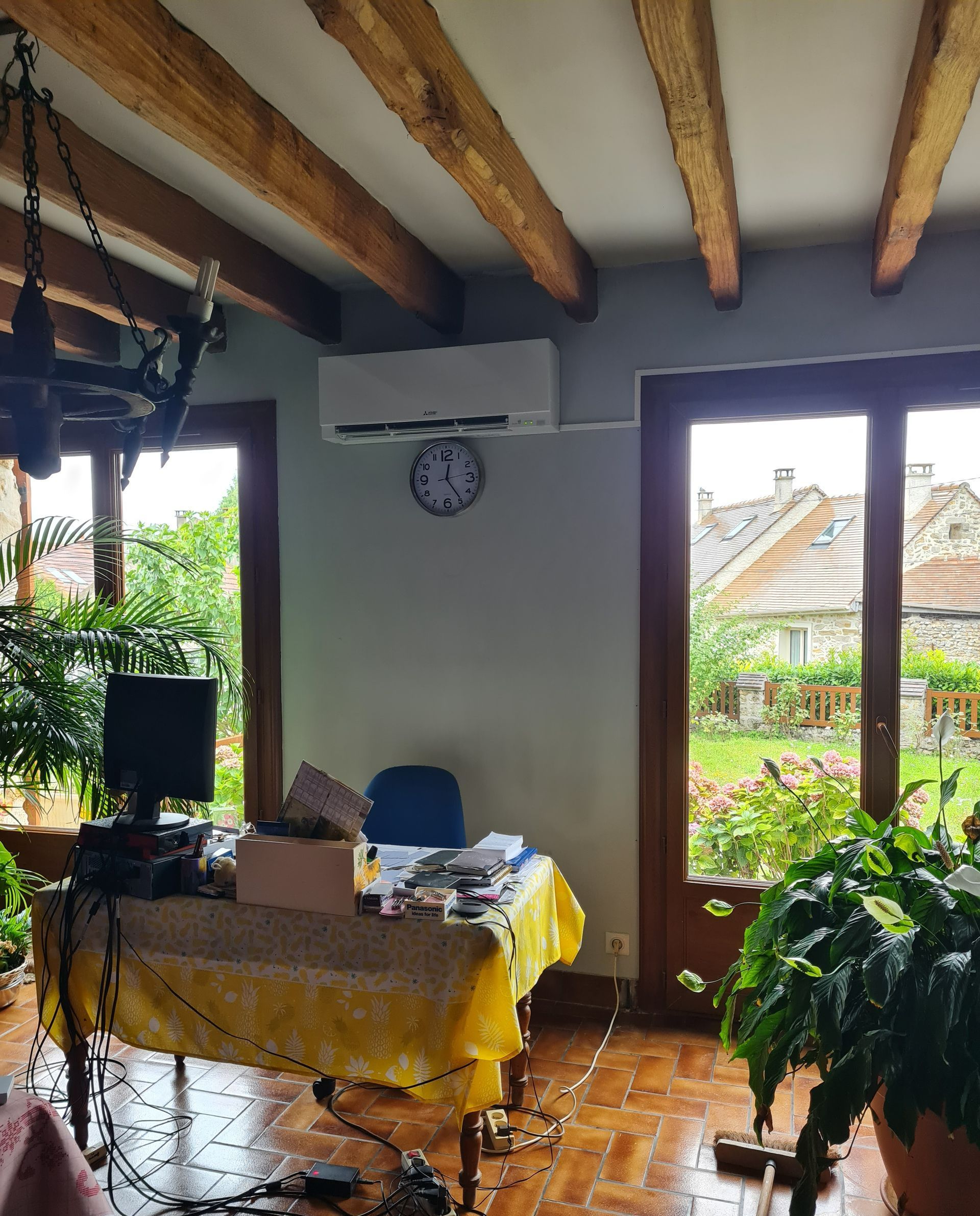 Climatisation mise en place en haut d'un mur intérieur de maison entre deux portes-fenêtres, sous un poste de travail